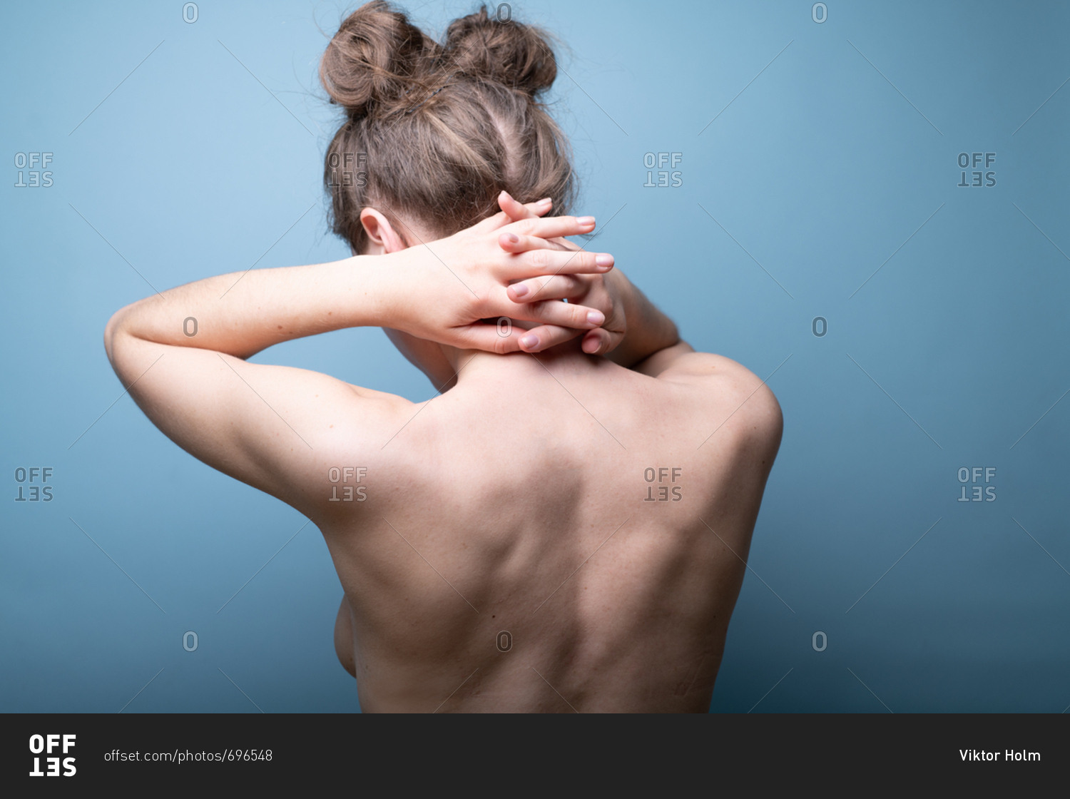 Female with pigtail hair buns putting hands behind neck on blue background