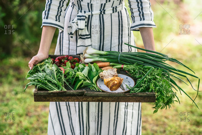Woman in striped dress presenting tray of seasonal spring produce from the garden