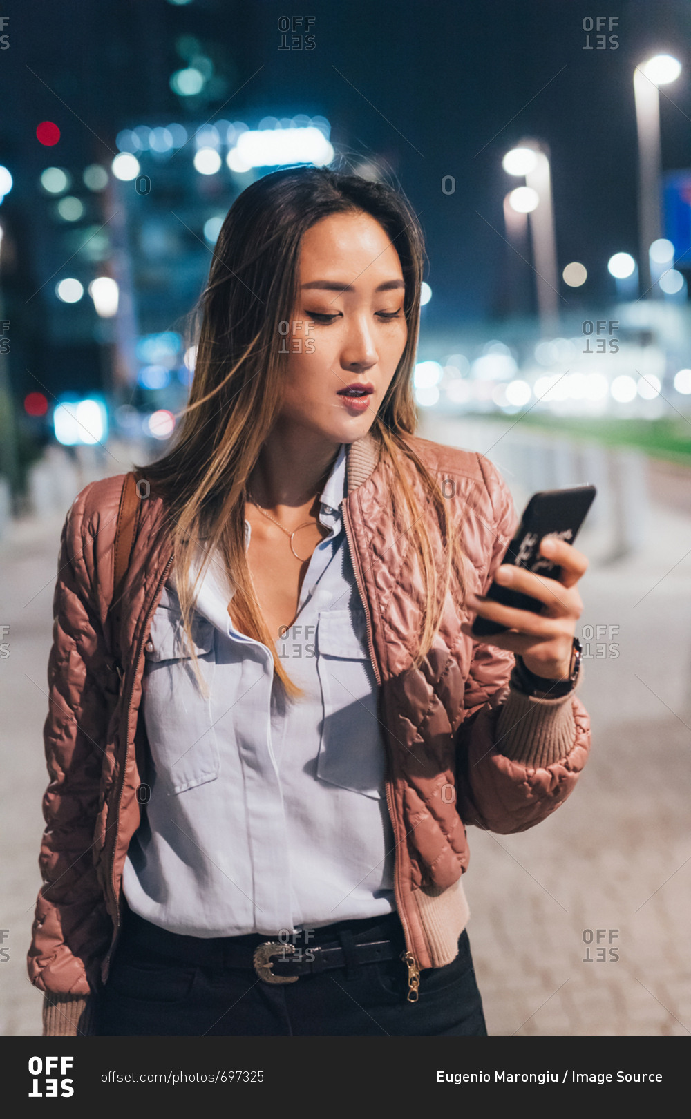 Woman standing outdoors, at night, using smartphone