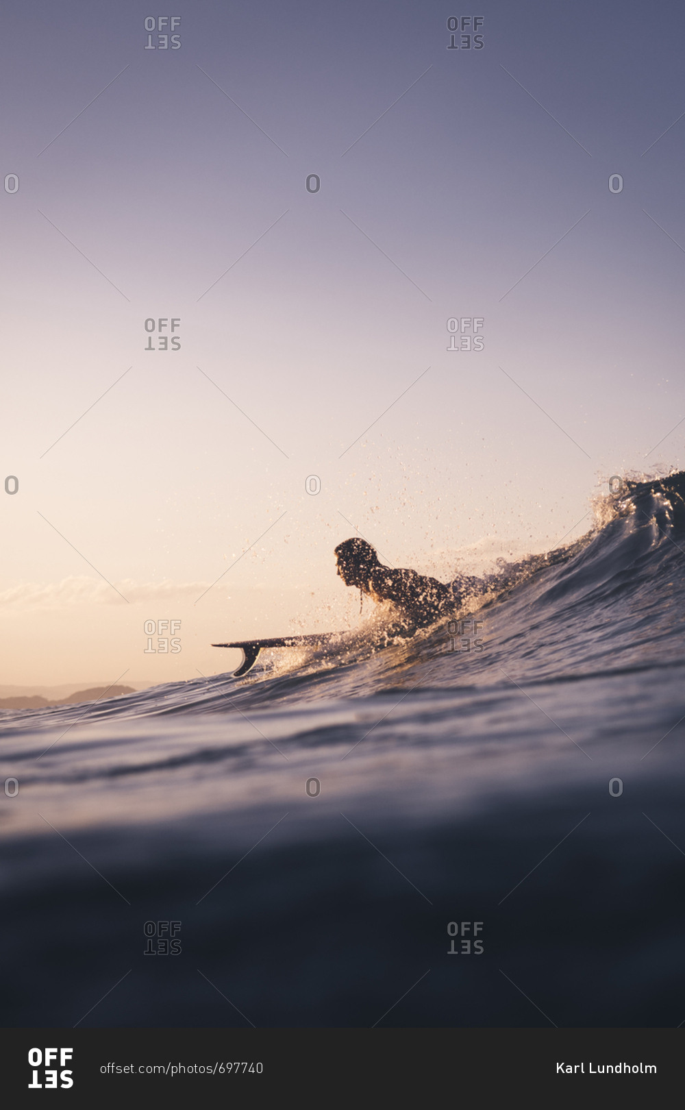 Surfer lying on surfboard while wave is forming and water splashing