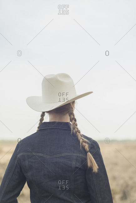 Rear view of cowgirl with braids in jeans jacket in field