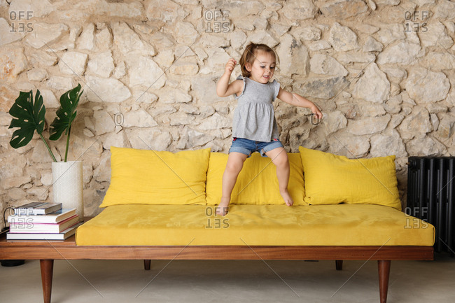 Little girl jumping on vibrant couch in retro decorated living room