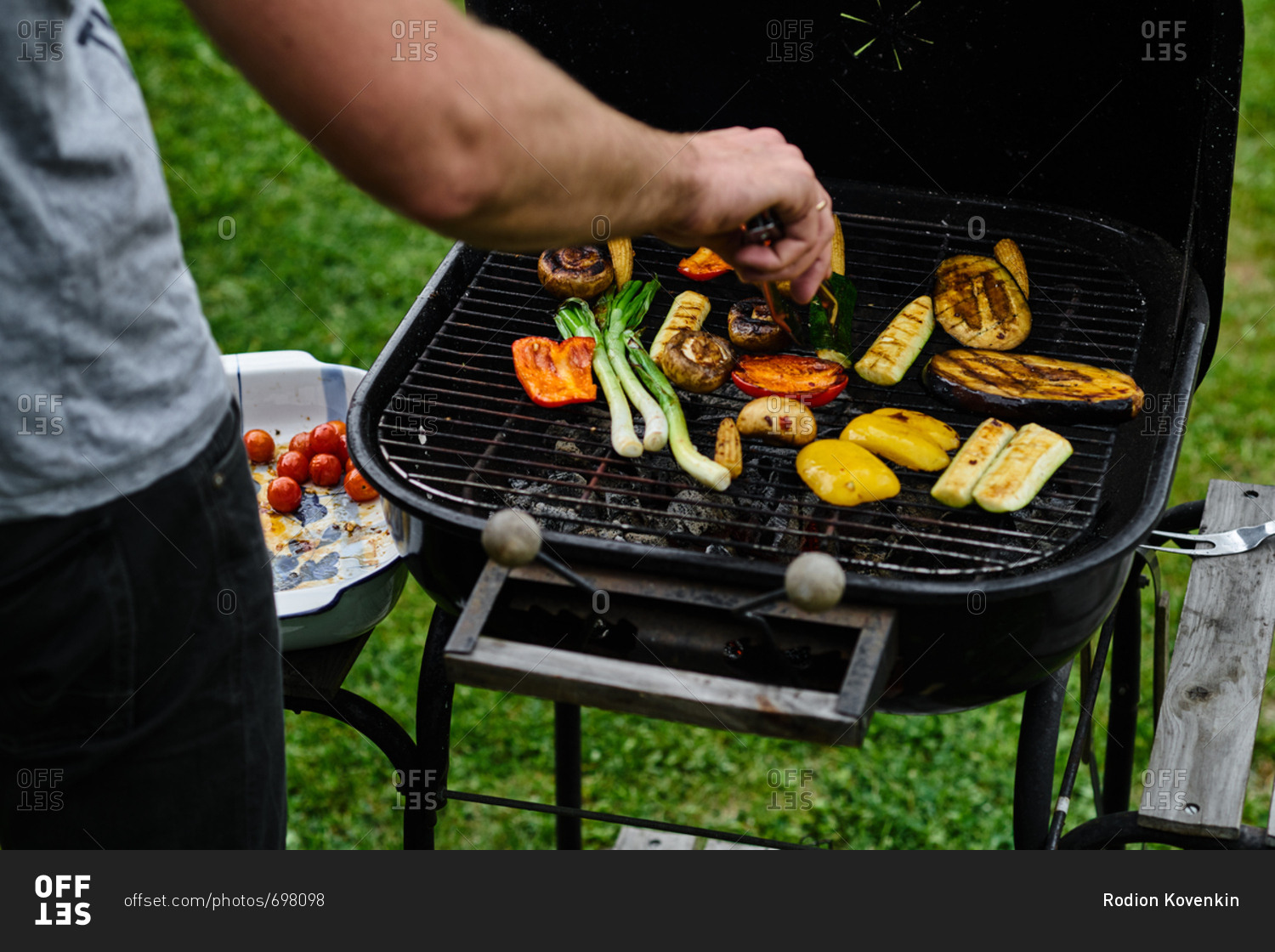 View from behind of man's arm using tongs to turn vegetables on the grill