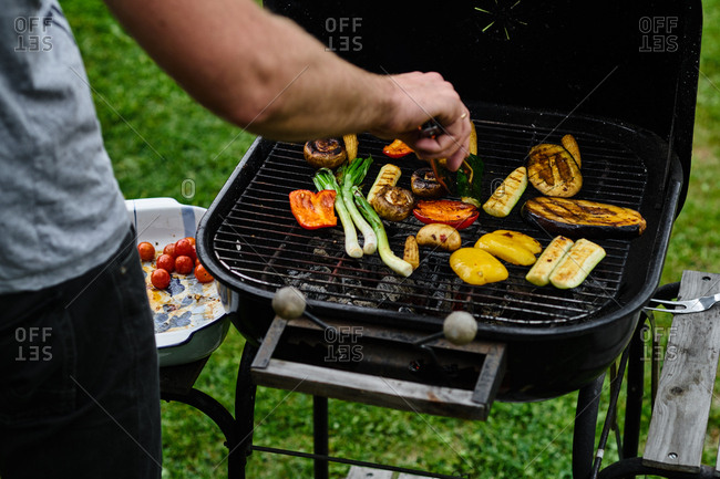 View from behind of man\'s arm using tongs to turn vegetables on the grill