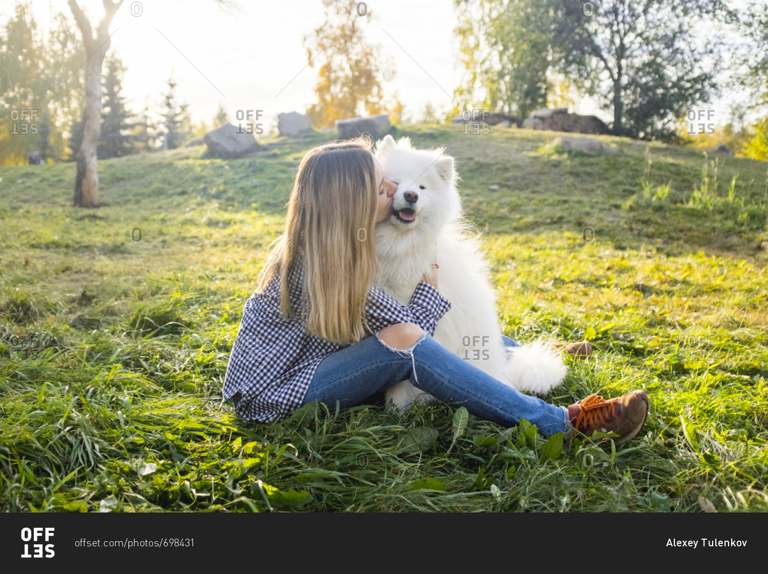 Woman sitting in a meadow kissing her pet Samoyed dog