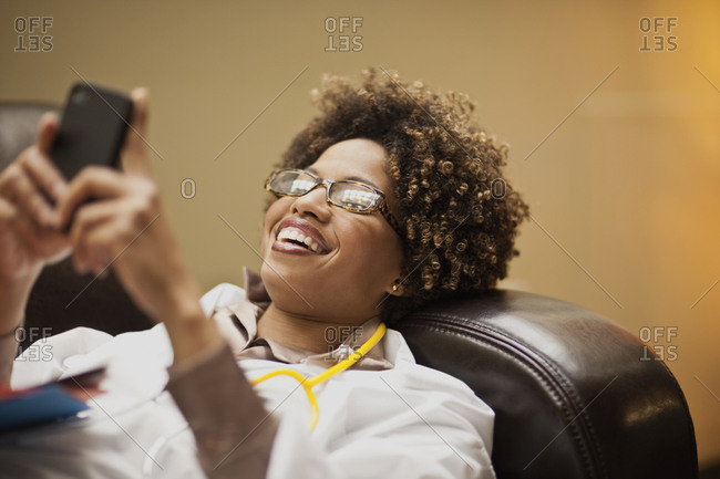 Female doctor taking a break, and text messaging on a sofa