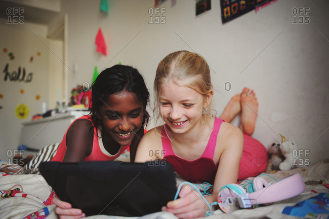 Two young girls hanging out on bed looking at screen of tablet device