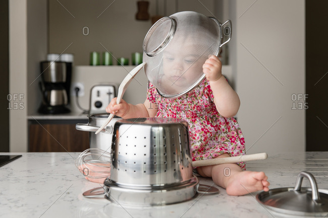 Baby sitting on kitchen counter playing with kitchenware