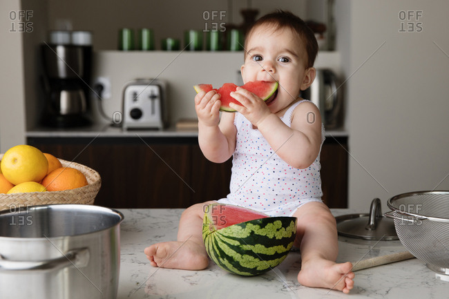 Baby sitting on kitchen counter with strainer on his head Stock Photo