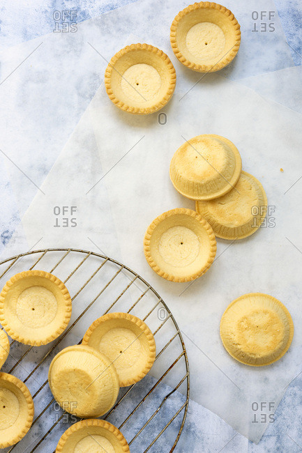 Small baked pastry tartlet cases cooling on a wire rack and baking paper.