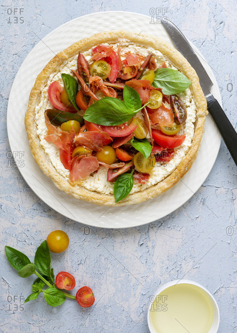 Round tart filled with cherry tomatoes, pancetta, feta cheese and basil on a plate with a knife.
