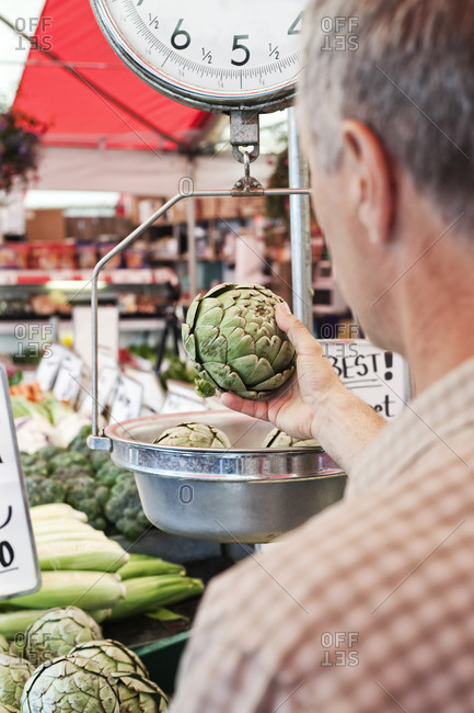 Over the shoulder view of man weighing artichoke at a fruit and vegetable market
