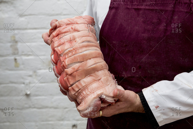 Close up of butcher wearing apron holding large rolled pork belly