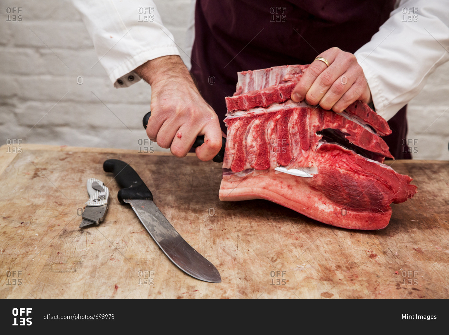 Close up of butcher wearing apron standing at a wooden butcher\'s block, butchering piece of pork loin