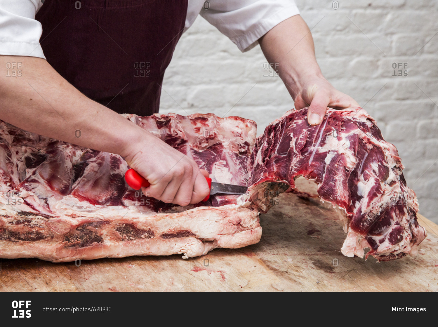 Close up of butcher wearing apron standing at a wooden butcher\'s block, butchering beef forerib