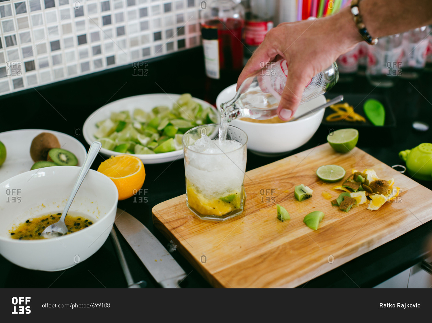 Person preparing a mixed drink with passion fruit, kiwi, and lime