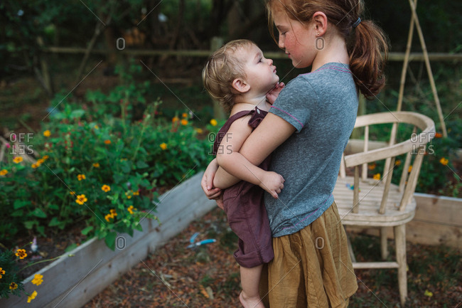 Older sister carrying baby sibling in garden