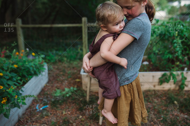 Big sister tenderly holding baby sibling in backyard