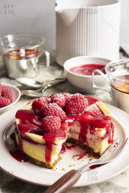 Homemade mini cheesecake with swirl of raspberry sauce topped with fresh raspberries for tea