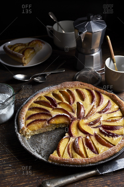 Homemade peach tart with custard and sweet yeast dough in dark rustic table setting