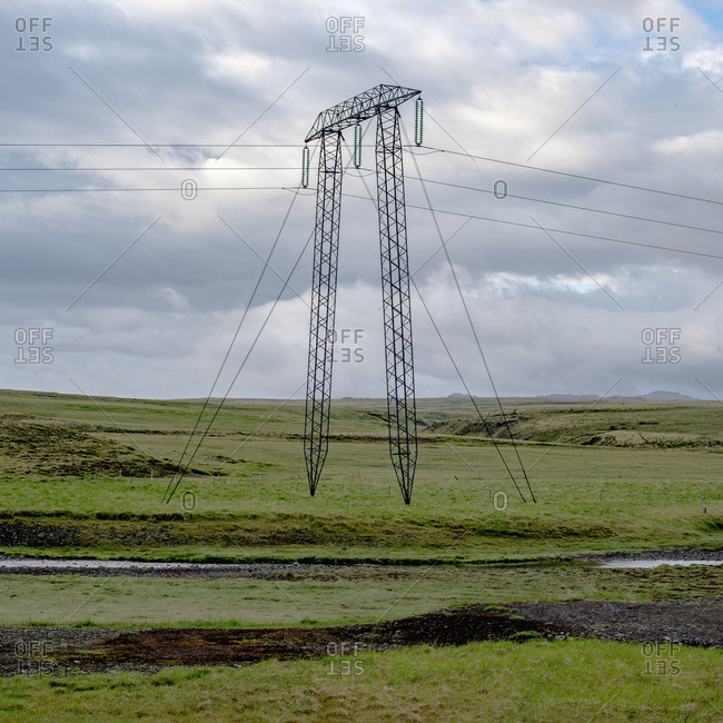 Electricity pylon on green field against cloudy sky, Highlands, Iceland