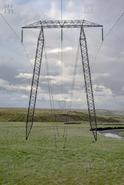 Row of electricity pylons on green field against cloudy sky, Highlands, Iceland