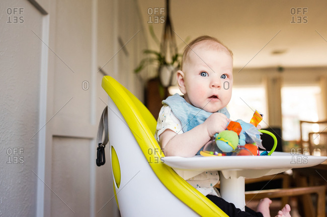 Little baby sitting in high chair with toys