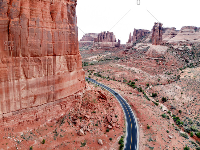 Aerial view of car driving along blacktop winding through red hued buttes in Arches national Park, Utah