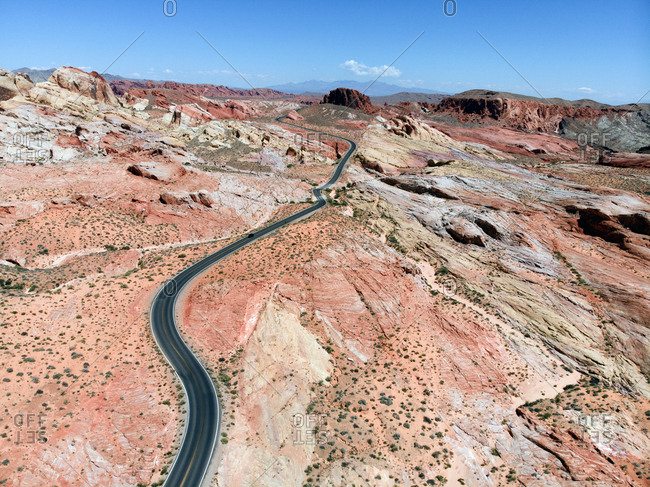 Aerial view of ribbon of immaculate black top road winding snaking through red hued landscape of Valley of Fire State Park, Nevada