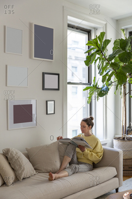 Woman Reading Magazine While Relaxing On Sofa At Home Stock Photo
