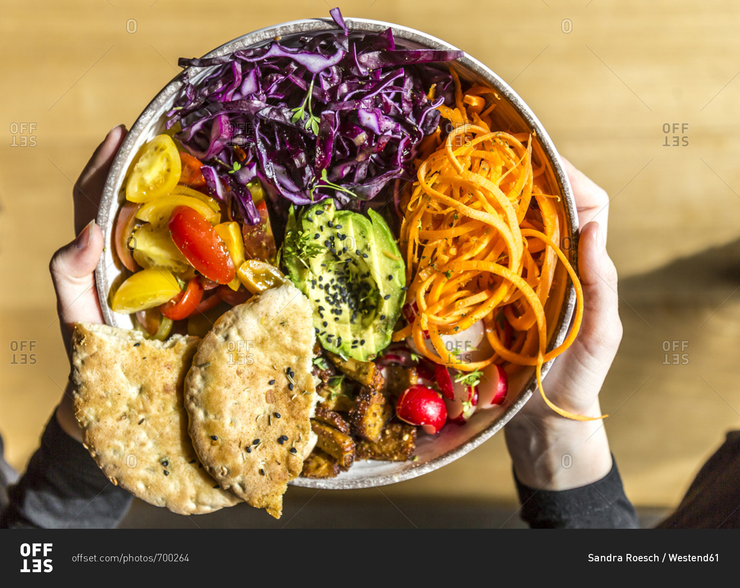 Girl holding veggie bowl with tomato- tofu- red cabbage- avocado- carrot- red redish- cress- black sesame and pita bread