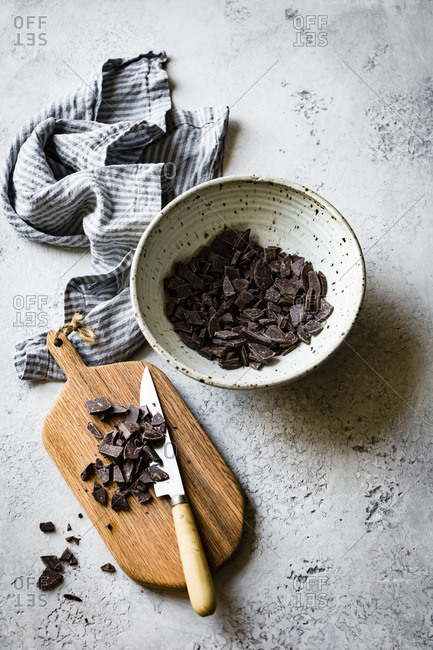 Chopped chocolate in a ceramic bowl, alongside a chopping board with knife