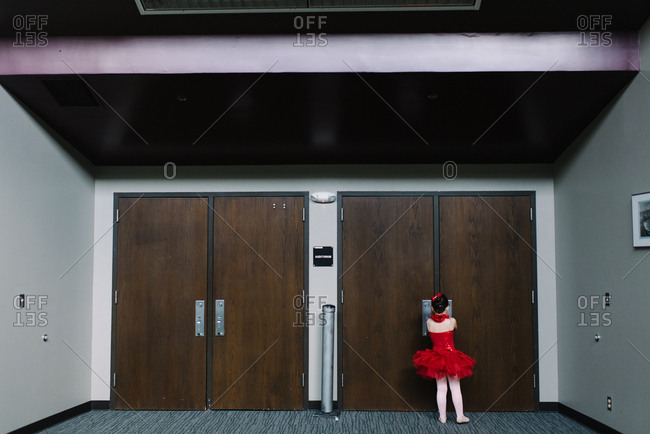 Little girl behind doors backstage wearing ballet costume
