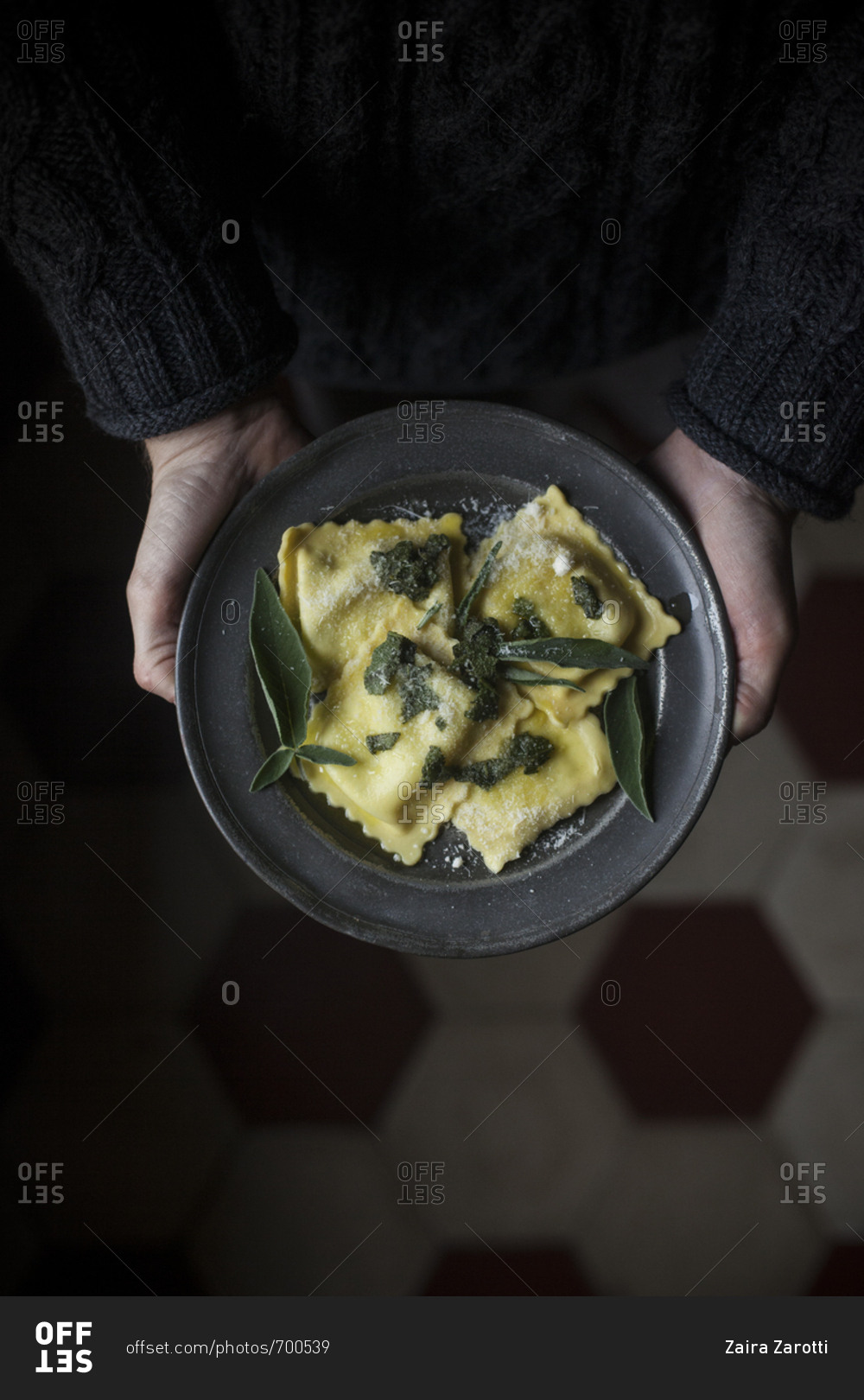 Overhead view of a person holding a dish of homemade ravioli seasoned with butter, sage and Parmesan cheese