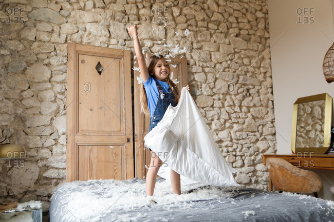 Little girl throwing feathers from a pillow into the air