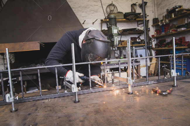 A blacksmith wears safety gear and is welding a metal construction in a metalsmith's workshop
