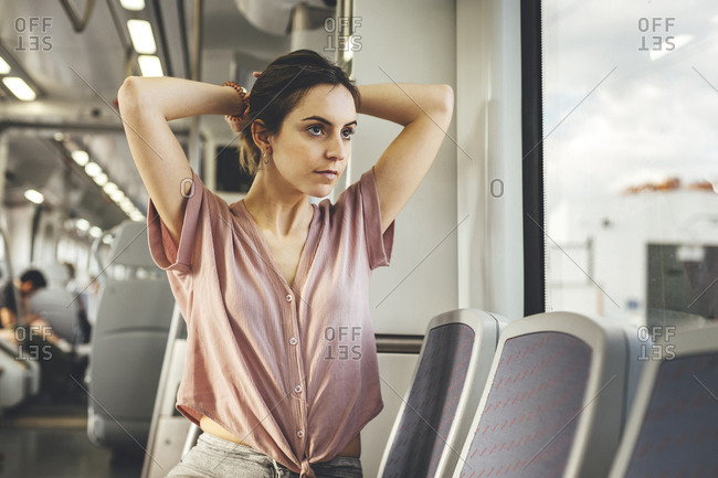 Young Woman Sitting In Train Carriage Tying Hair Up Looking Out Of