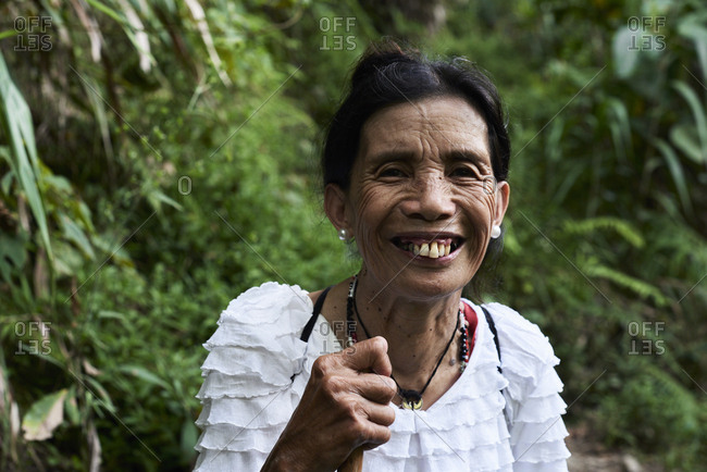 Batad, Philippines - March 4, 2018: Portrait of a happy senior filipina lady smiling at camera in the jungle with walking stick.