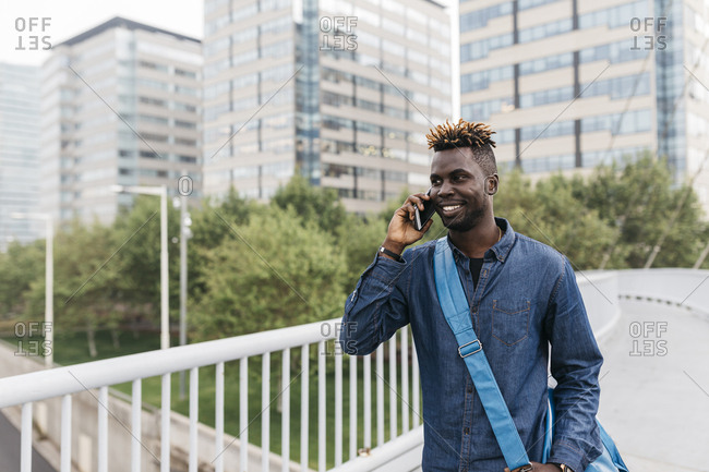Young black man talking on mobile phone in Barcelona with city skyscrapers on background