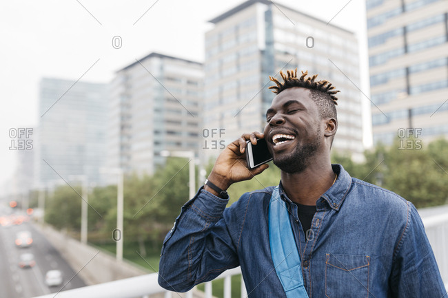 Young black man talking on mobile phone with a big smile in Barcelona with city skyscrapers on background