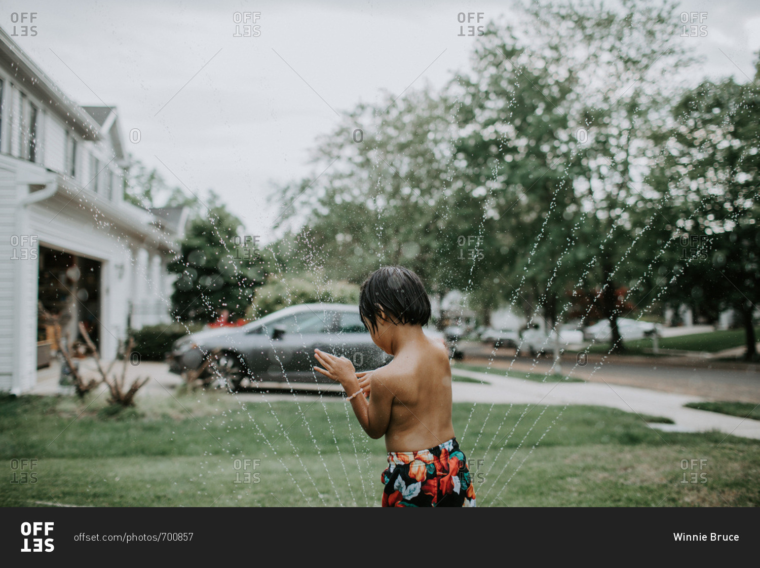 Boy playing in sprinklers in front yard