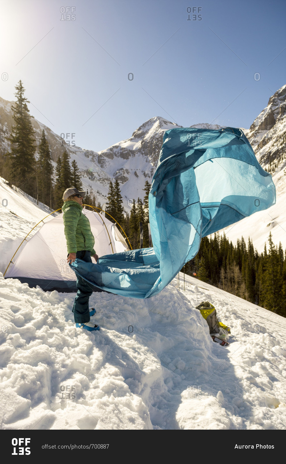 Adult woman packing up tent after winter camping in snowcapped Arastra Gulch mountain pass, Silverton, Colorado, USA