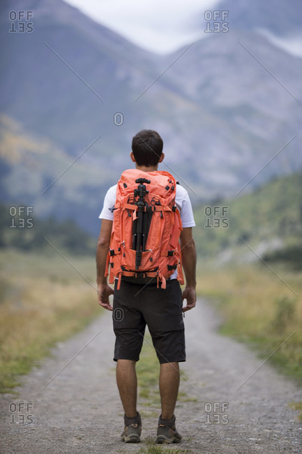 Rear view of male hiker standing with backpack on empty dirt road of Otal Valley, Torla, Huesca, Spain
