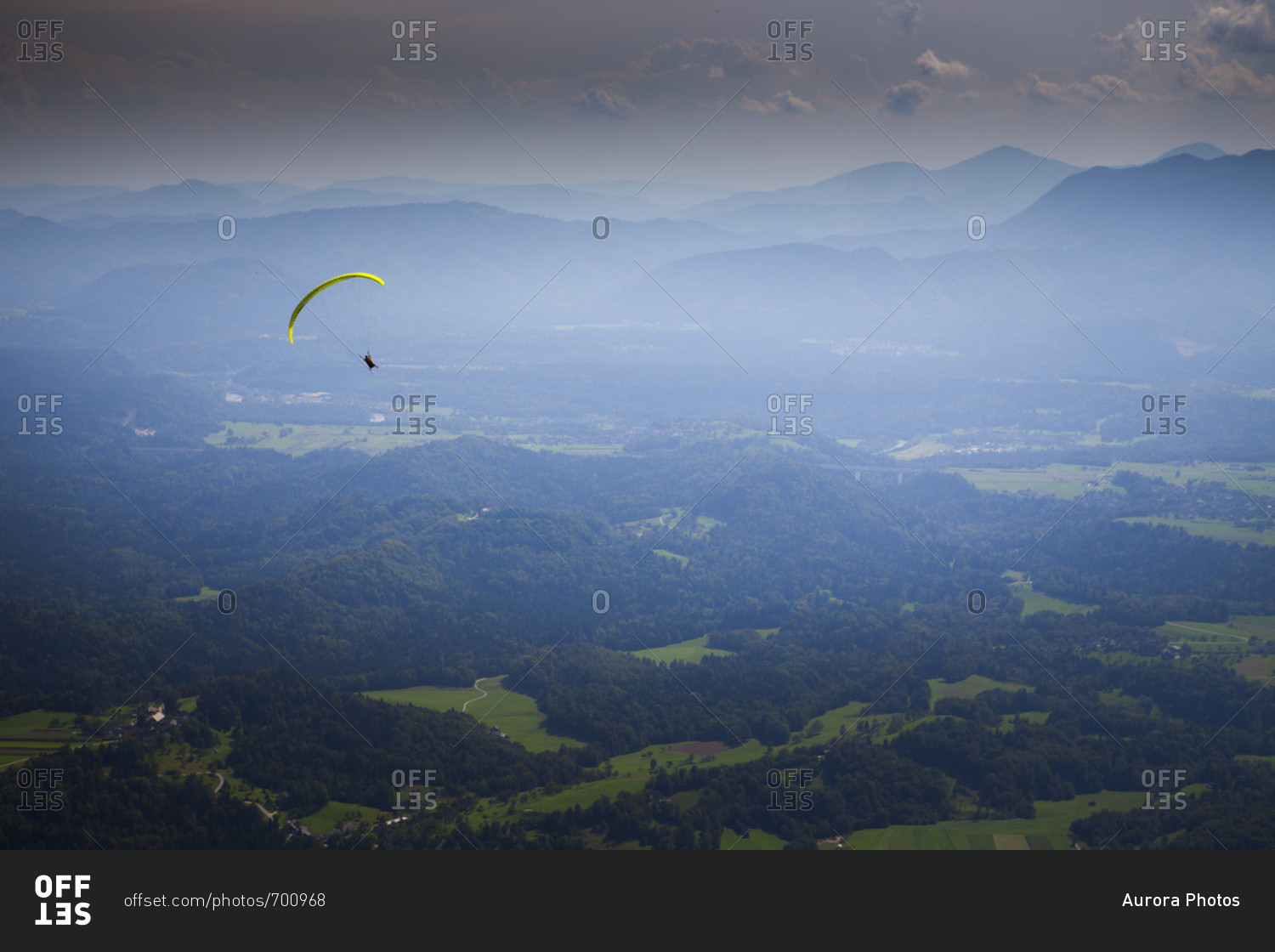 Distant view of a paraglider flying high above the mountain valley of Begunje and Radovljica, after taking off from Dobrca mountain, Upper Carniola, Slovenia