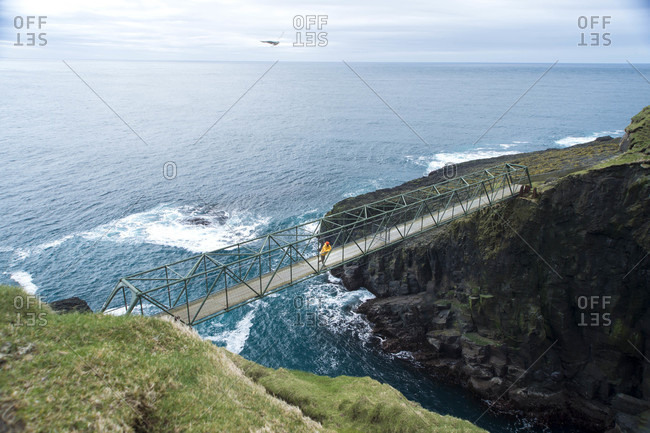 Adventurer stopping on bridge between two of Faroe Islands to enjoy view