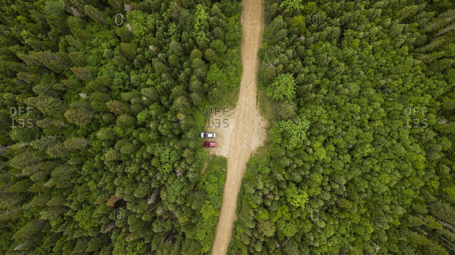 Aerial view of two cars in parking lot along dirt road surrounded by forest, Gaspe, Quebec, Canada