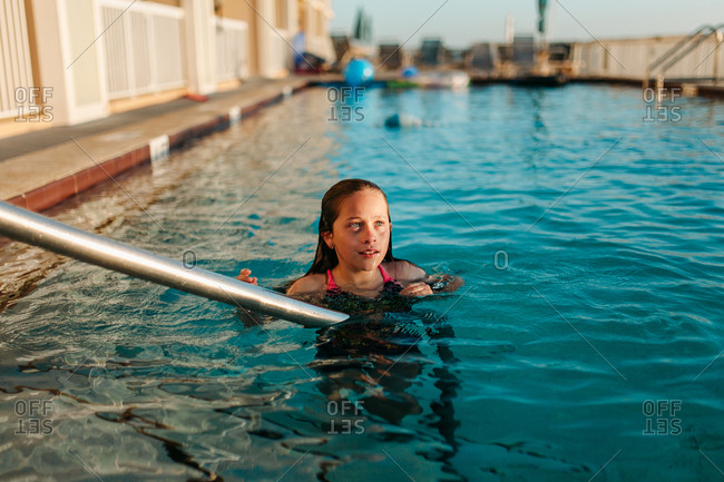 Girl swimming alone in hotel pool at sunset