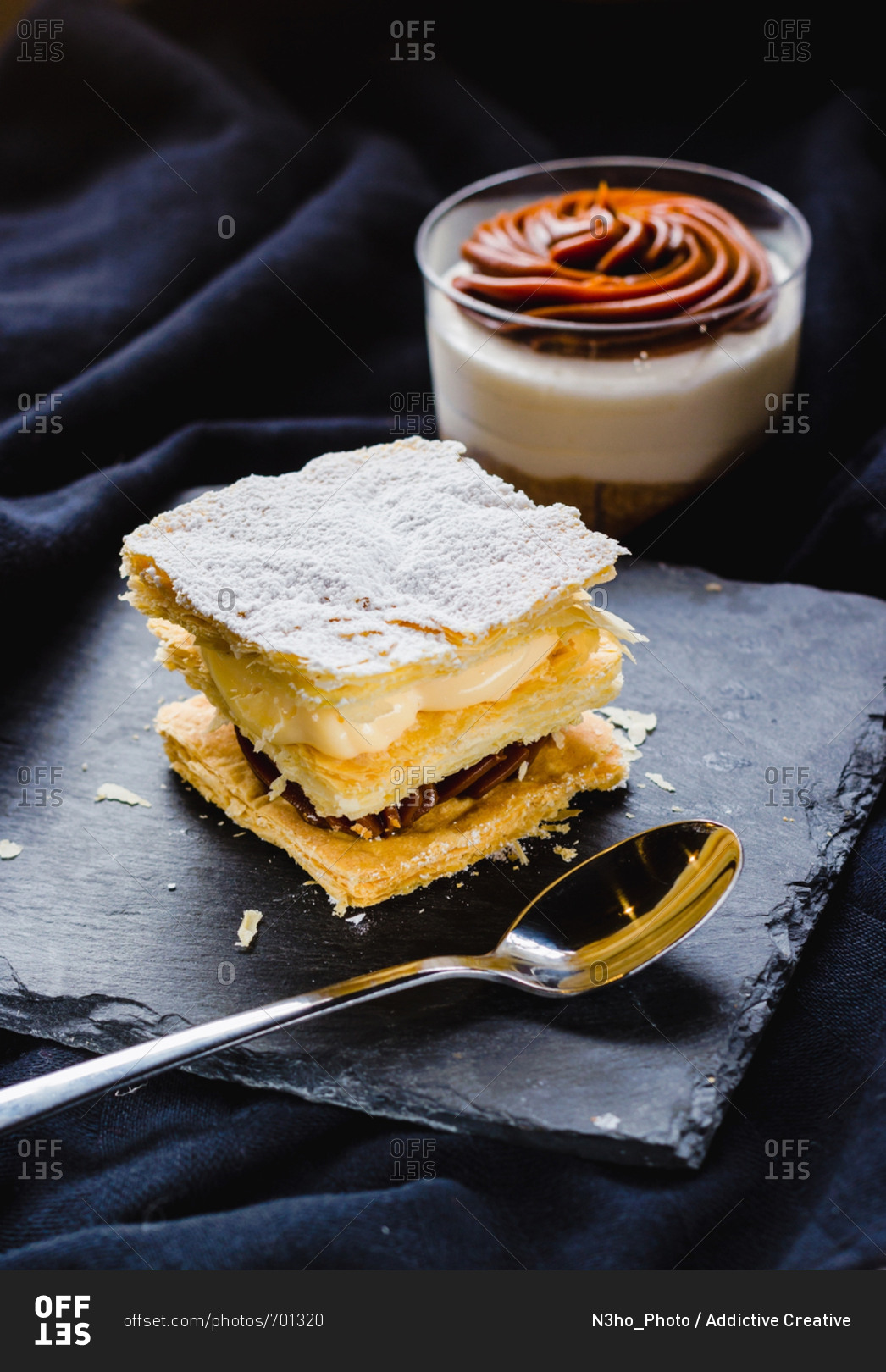 Close-up of puff pastry dessert with creams on plate and dessert in cup composed on soft textile