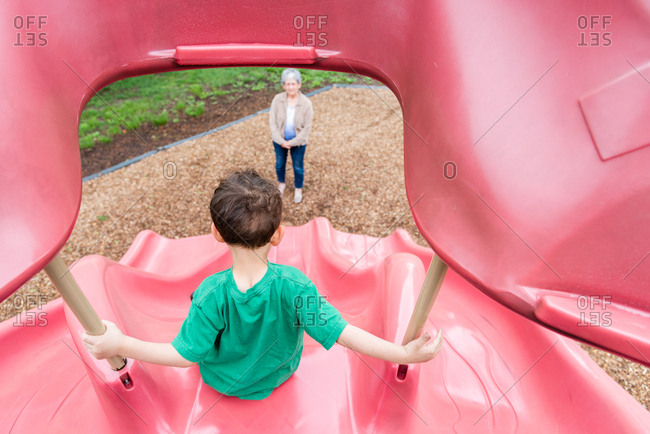 Grandmother watching boy slide down a slide
