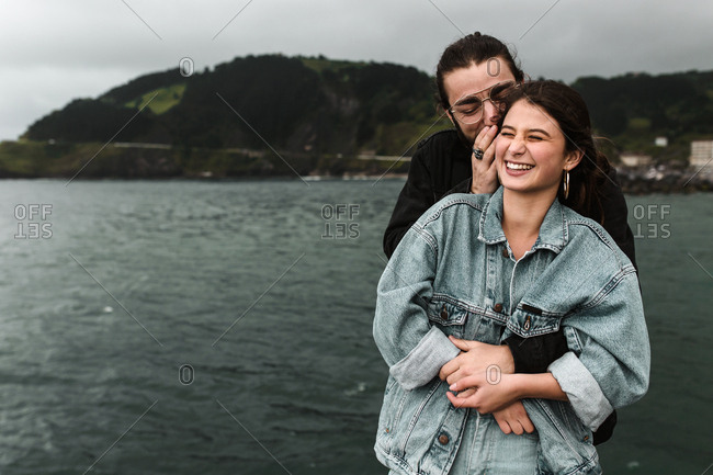 Tourist couple telling playful secrets at the stormy beach